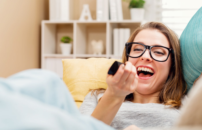 woman with glasses laughing while watching tv