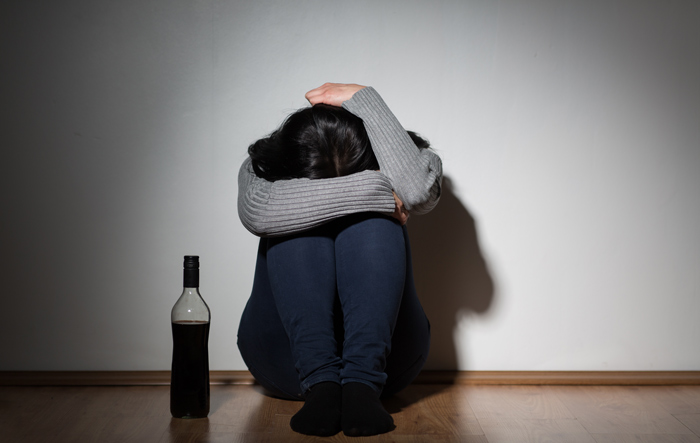 sad woman hugging knees to chest near bottle of liquor - women are