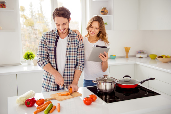 attractive young couple cooking together in their kitchen - man is chopping vegetables - self-care