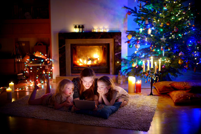 woman looking at a tablet computer with young relatives in front of Christmas tree and fireplace - peace