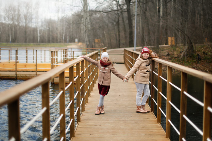 two little girls dressed for cold weather, holding hands and looking sad - adverse childhood experiences