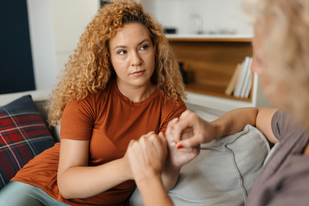 woman sitting on the couch holding her friend's hands - supporting friends