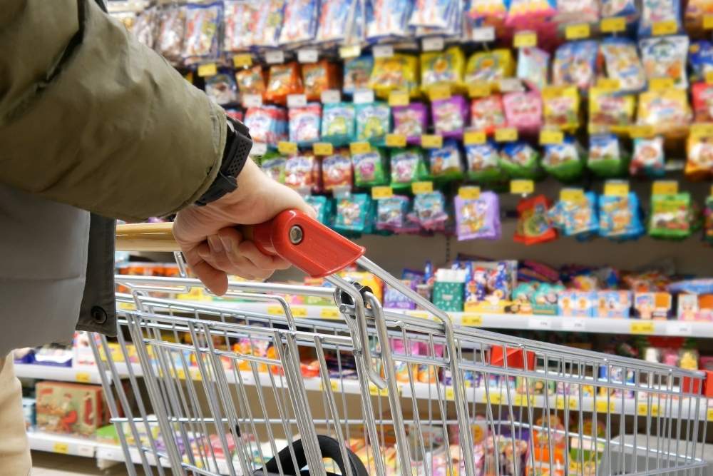 A shopper pushes a grocery cart down an aisle filled with colorful packaged candy and sweets on display.