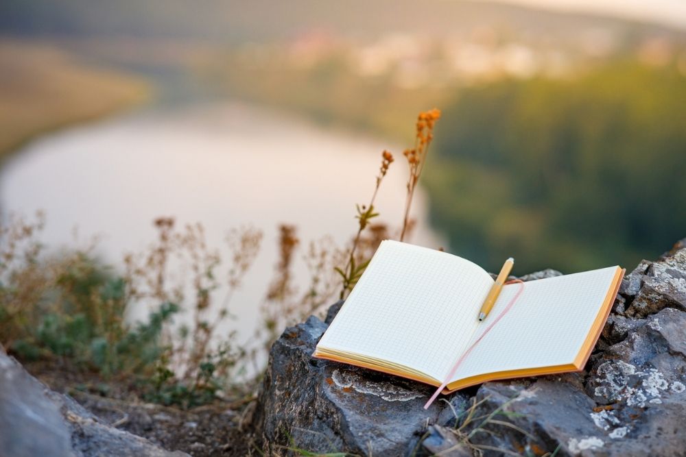 An open empty book with a fountain pen outdoors, the background is a blurred river and forest