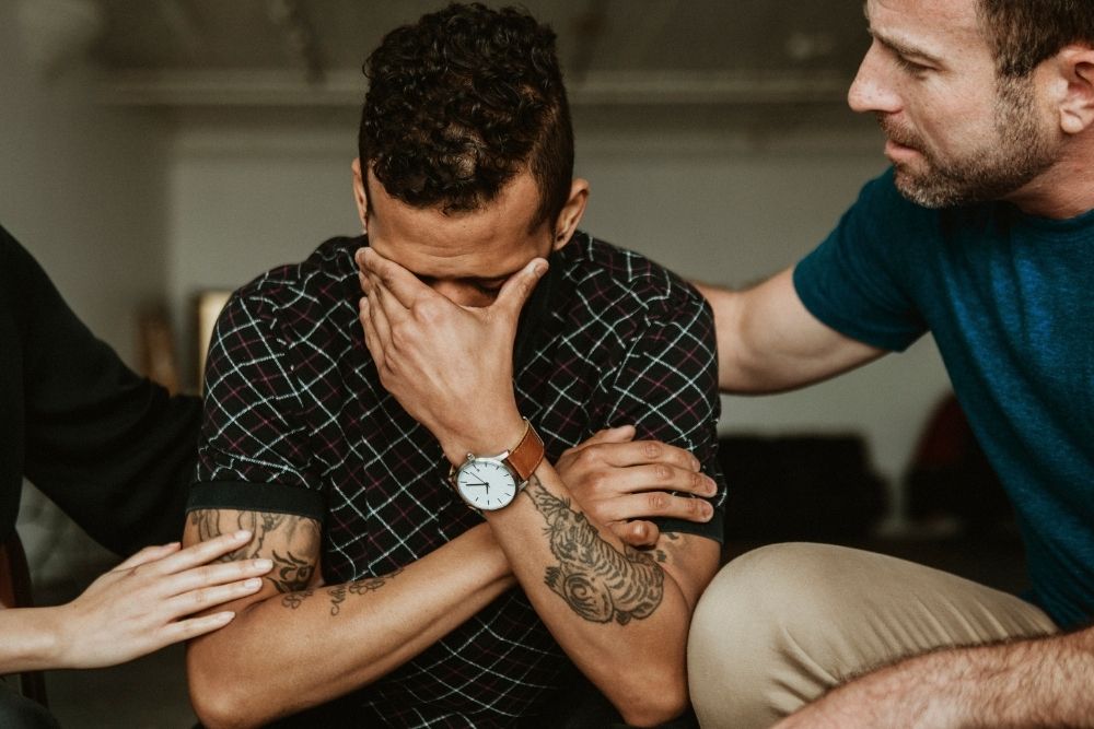 Willingway - Types of Addiction and How Willingway Can Help. A man hangs his head in his hands as two people comfort him.