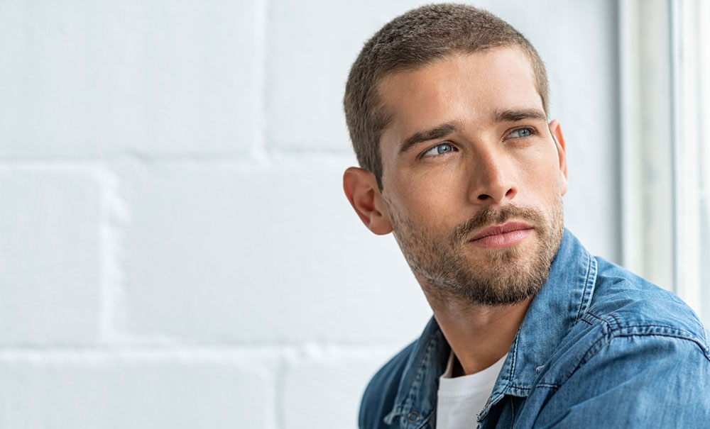 portrait of a young man with a beard looking out of a window